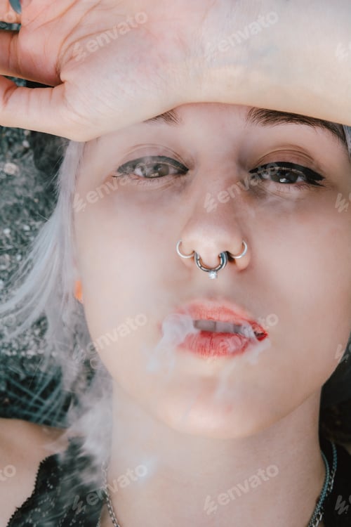 Preview: Portrait of a blonde female lying on the ground and smoking with her hand on her face