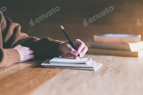 Preview: Closeup image of a woman writing on blank notebook on wooden table