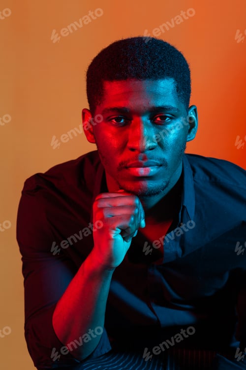 Preview: Close up portrait of a young african american man on orange neon studio background