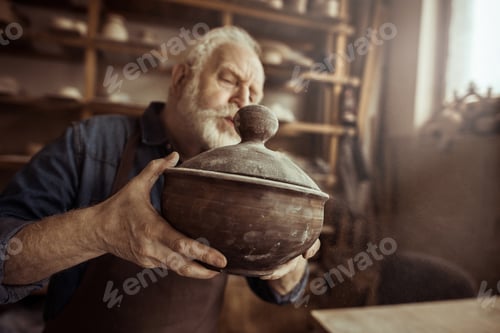 Visualização: Ceramista sênior no avental examinando tigela de cerâmica na oficina