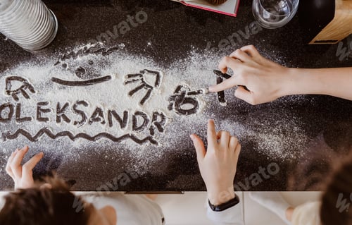 Preview: Children playing with baking flour on kitchen table at home drawing pictures