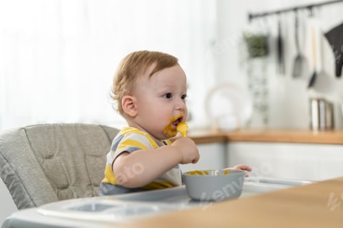 Preview: Caucasian young baby toddler sitting alone on children chair eating healthy foods in kitchen