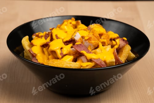 Preview: Black bowl of loaded fries topped with creamy sauce and grilled chicken on a wooden table