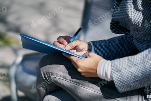 Preview: Female sitting on a park bench writing some notes captured on a sunny day
