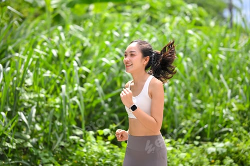 Preview: Active woman jogging outdoors in nature, smiling and enjoying a healthy lifestyle on a sunny day