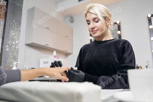 Preview: Charming Caucasian female master working with nail file in nail salon