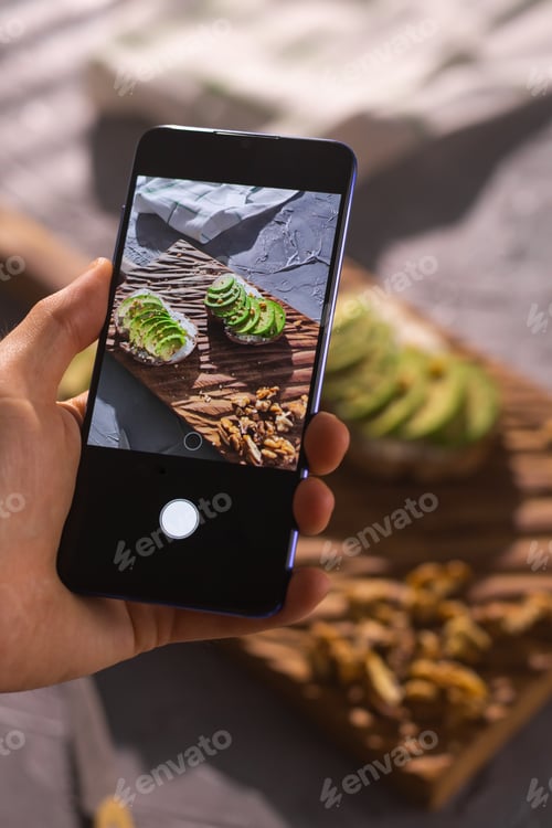 Preview: Smartphone taking picture from organic healthy sandwiches with avocado. Man hand.