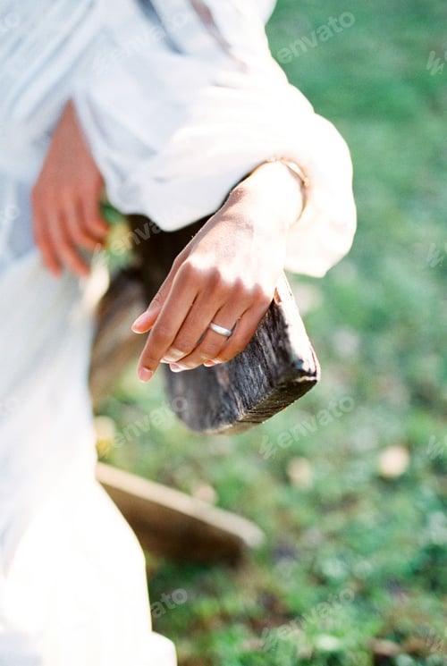 Preview: Woman hand with a ring on her finger lies on the back of a wooden bench. Close-up