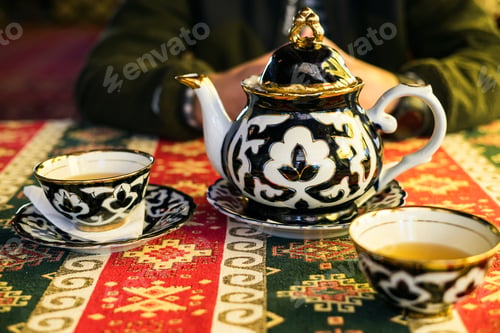 Preview: Traditional tea ceremony setup with a patterned Uzbek teapot and cups on a colorful table runner