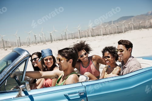 Preview: A group of friends in a pale blue convertible driving on a plain surrounded by mountains.