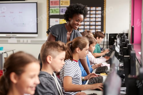 Preview: Teacher Helping Female Pupil Line Of High School Students Working at Screens In Computer Class