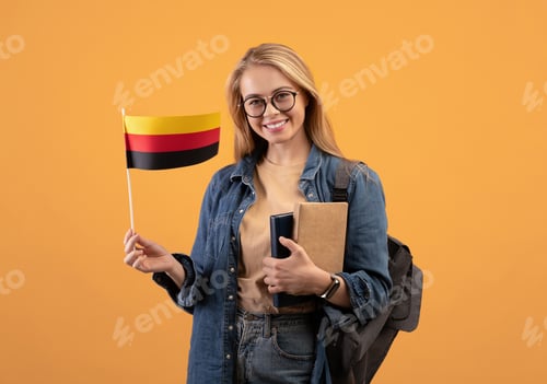 Preview: Happy young blonde lady student in casual with glasses, backpack and books holding small flag of