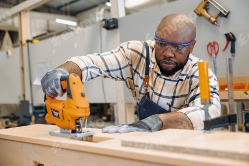 Preview: black african male carpenter joiner using Jig Saw wood panel cutter to cut making furniture panel
