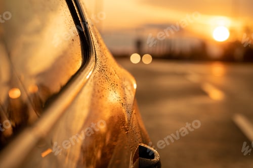 Preview: Closeup of raindrops on a car at sunset with surroundings reflecting on the side