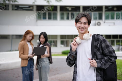 Preview: Happy and smiling asian student holding headphones with friends working on a laptop