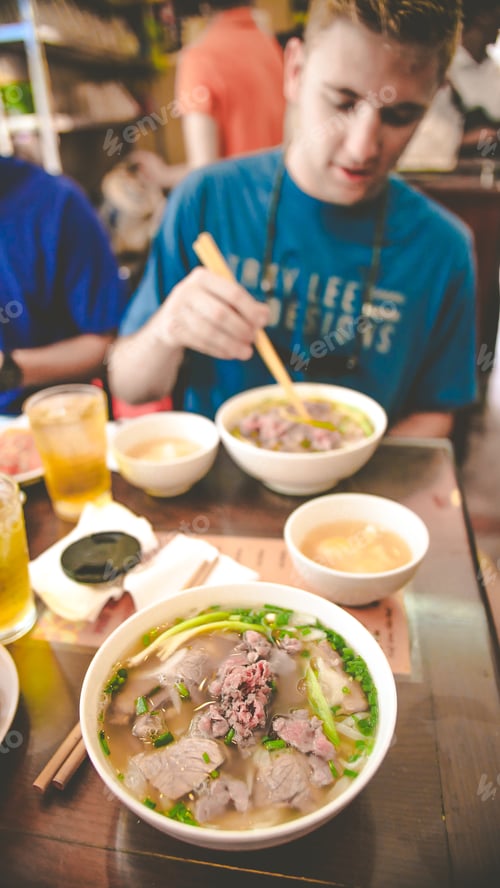 Preview: Vertical shot of a male eating pho food in Vietnam