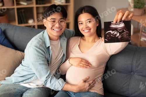 Preview: Joyful japanese couple showing sonogram photo of their baby indoor