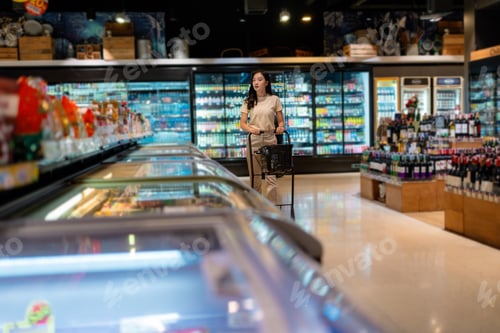 Preview: Young woman pushing shopping cart in supermarket looking for groceries