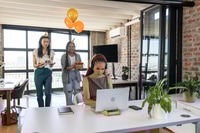 Preview: Colleagues surprising woman with cake and balloons in modern office celebration