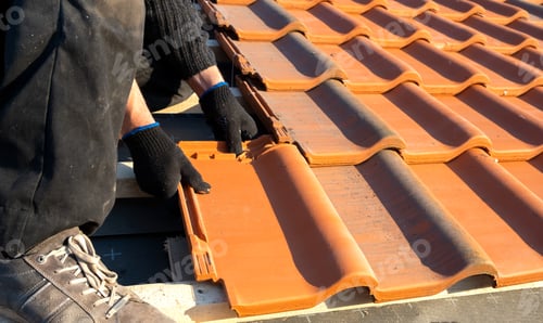 Preview: Closeup of worker hands installing yellow ceramic roofing tiles mounted on wooden boards covering