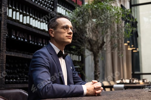 Preview: adult man in stylish suit sitting at restaurant in front of wine storage shelves