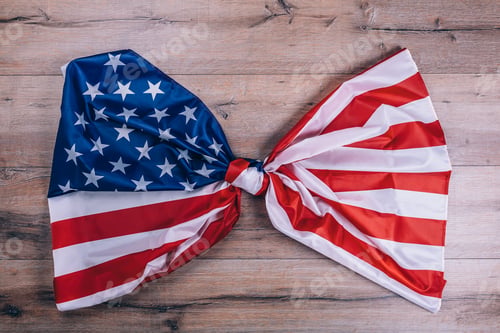 Preview: American flag, tied in a knot, on dark wooden wall. Visual concept of preparation for Independence
