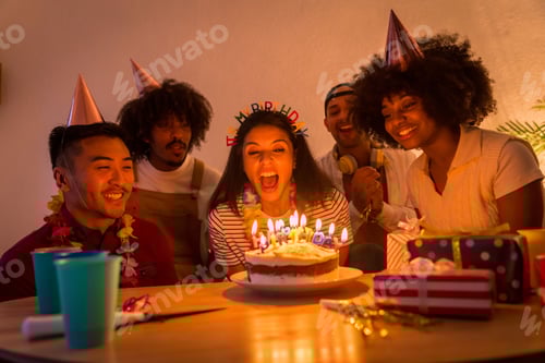 Preview: Multi-ethnic group of friends at a birthday party, celebrating the birthday with the lights off