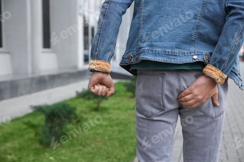 Preview: Man suffering from hemorrhoid pain outdoors, back view