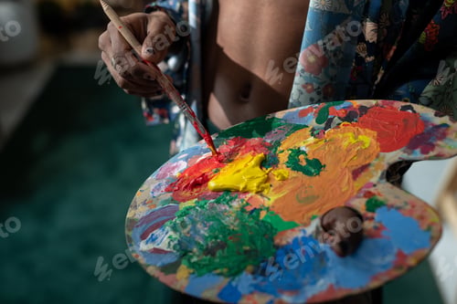 Preview: Hands of young non-binary man mixing acrylic paints on palette