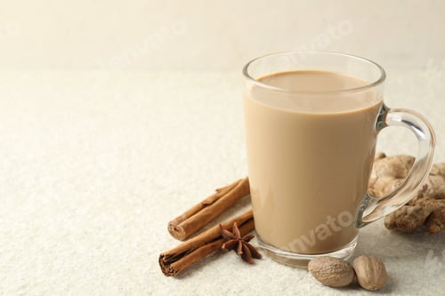 Vista previa: Té masala aromático en taza de vidrio y especias sobre mesa con textura blanca, primer plano. Espacio para texto