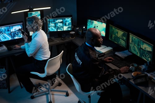 Preview: Middle Aged Caucasian Woman and Black Man Monitoring Security Cameras at Night