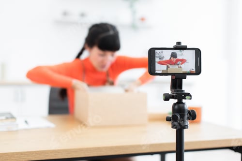 Preview: Caucasian female blogger creating unboxing video with smartphone camera