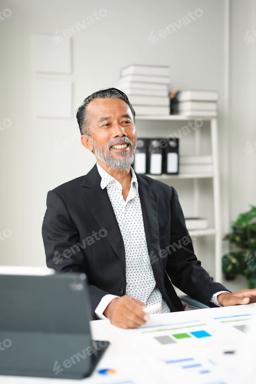 Preview: Happy mature businessman wearing suit sitting at desk in office working with documents