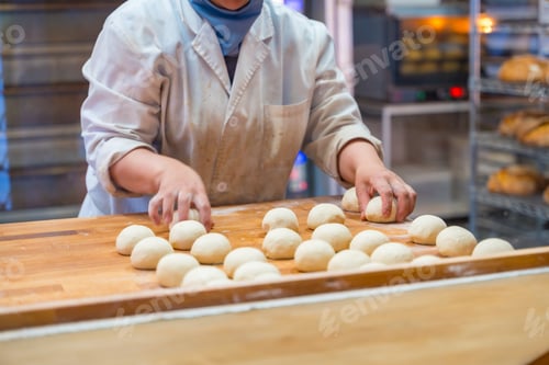 Preview: Woman breadmaker employee in the artisan bakery workshop preparing the dough in a circle