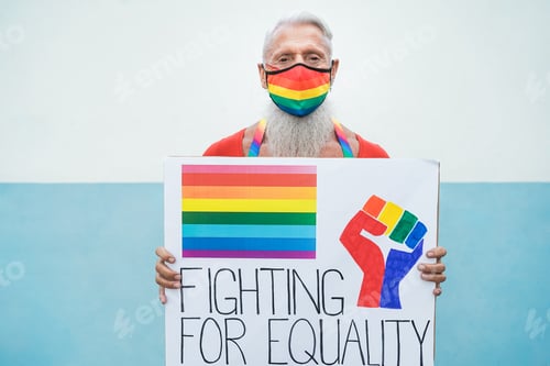Preview: Hipster gay senior man with rainbow mask holding banner at lgbt pride - Focus on face