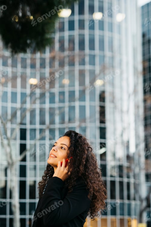 Preview: Businesswoman making a phone call in front of modern office building