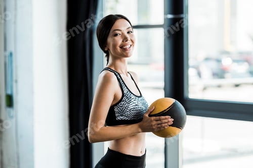 Preview: happy woman holding yellow ball and smiling in gym