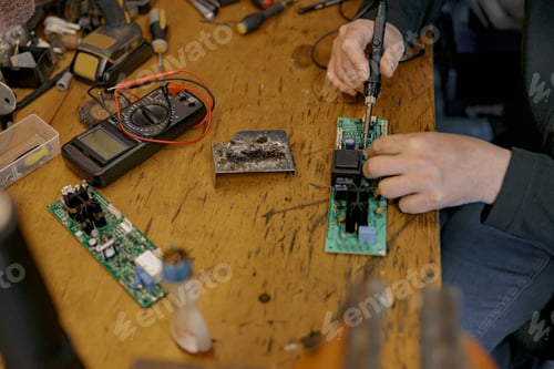 Preview: Close up of repairman hands is soldering circuit board of electronic device on the table