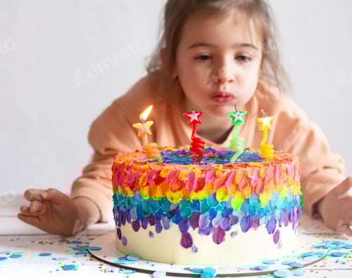Visualização: Menina soprando velas em um bolo de aniversário colorido.