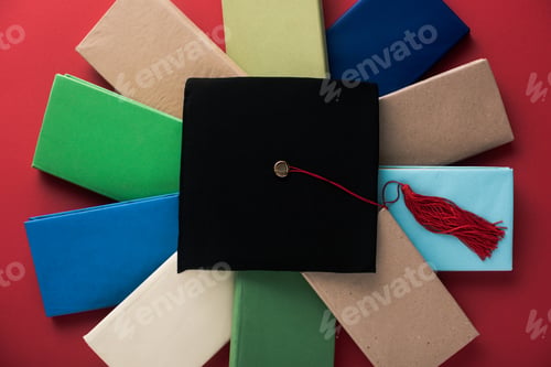 Preview: Top view of black graduation cap with tassel on books on red background