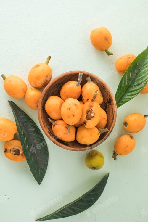 Preview: Ripe medlar fruit , Eriobotrya japonica, and green medlar leaves on wooden table. Top view