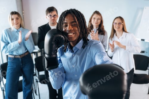 Preview: Black man is with boxing gloves. Group of young business people are in conference room