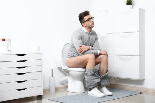 Preview: Man with glasses sitting on toilet bowl in bathroom
