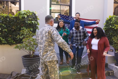 Preview: Happy diverse friends with flags welcoming home male soldier friend
