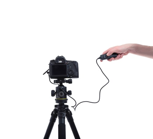 Preview: Camera with the lens on tripod. Hand presses the shutter or remote control unit