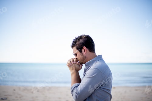 Preview: Shallow focus shot of a male near the beach with his hands near his mouth while praying