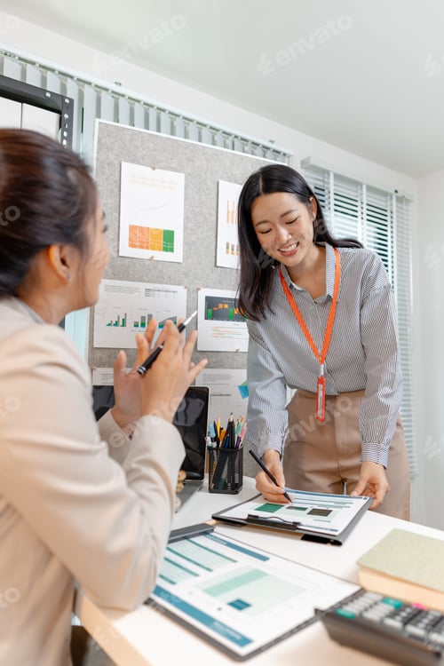 Preview: Two Asian businesswomen discussing company strategy together in a modern office