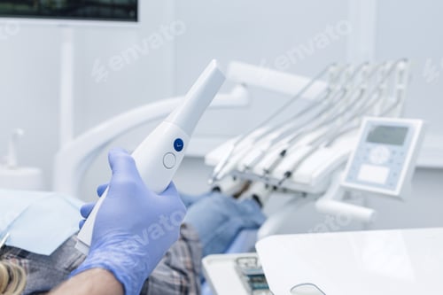 Preview: Gloved hand holding intraoral scanner for digital impression in modern dental clinic