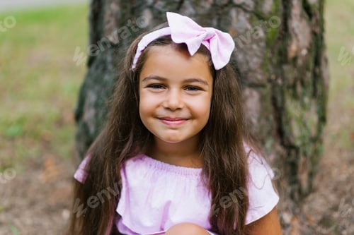 Preview: Happy Girl With a Pink Bow on Her Head and in a Pink Dress Looks at the Camera and Smiles