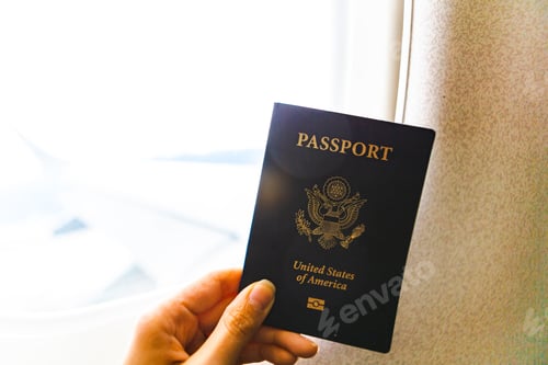 Preview: Woman’s hand holding a United States of America passport while on an airplane by the plane window